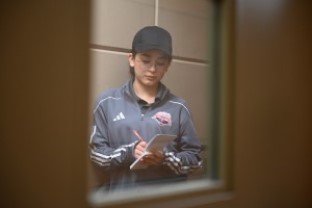 A youth academy student wearing a baseball cap takes notes in a notebook