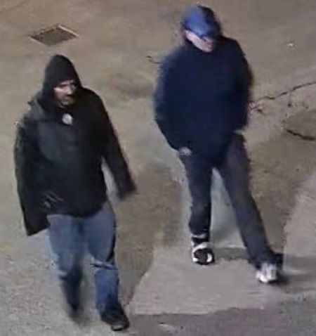 An image of suspect two and three walking. One man has his dark hood up and is wearing blue jeans, the other is in a blue ball cap. 