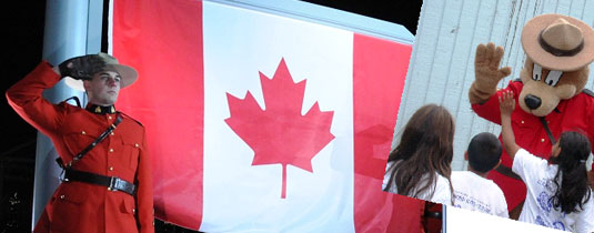 Un agent de la GRC et le drapeau canadien; ours prudent faisant un signe de la main à des enfants 